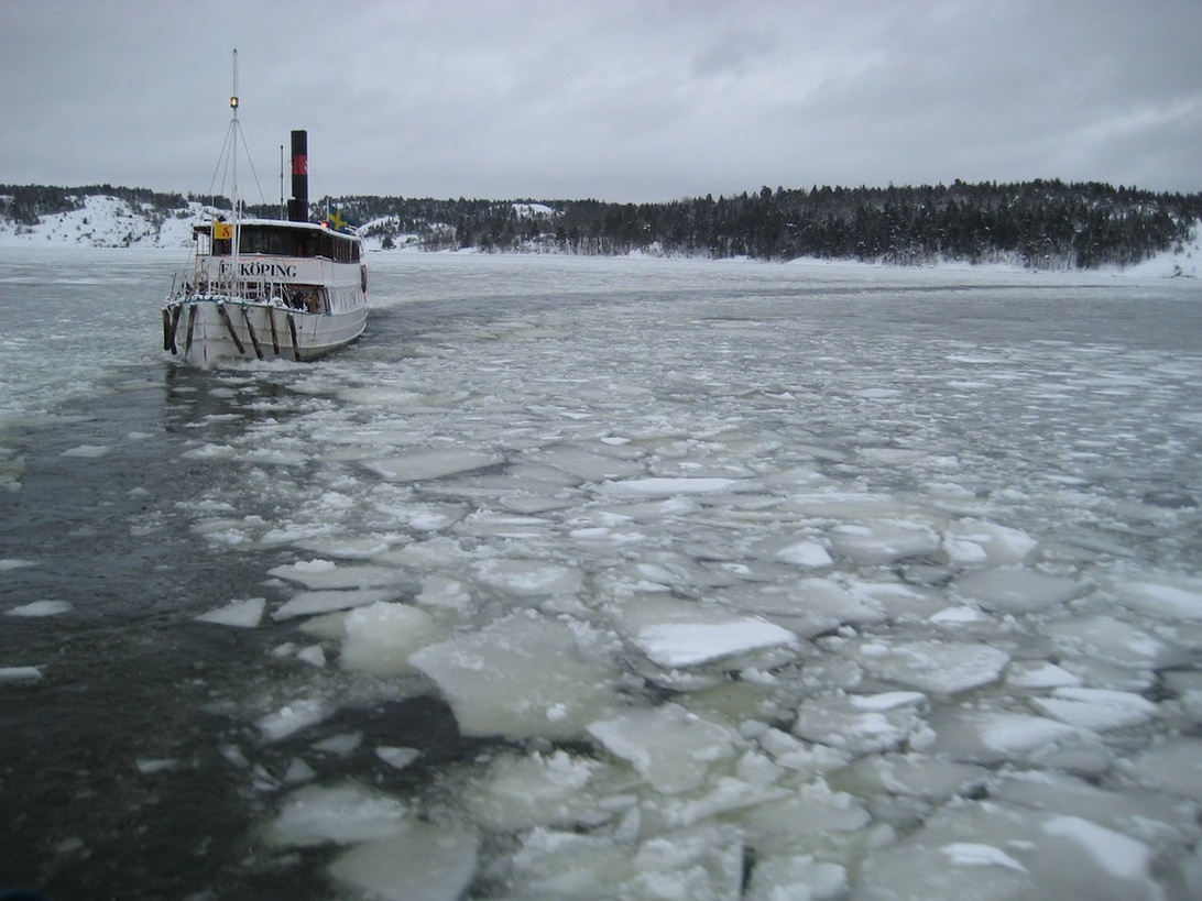 Ein kleines Passagierschiff navigiert durch teilweise zugefrorenes Wasser mit Eisschollen.